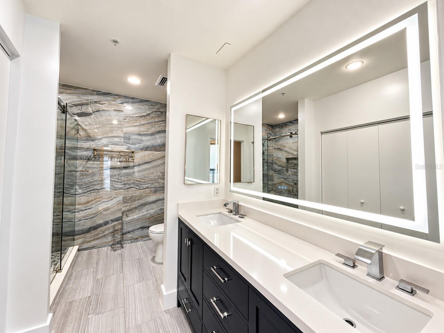 Primary bath vanity with waterfall faucets and an LED mirror in the Aspire penthouse